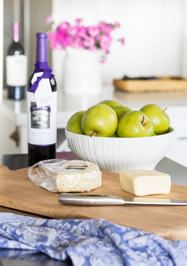 an island to a small kitchen with a wine bottle with a thank you gift tag tied on among a cheese board and bowl of green apples.