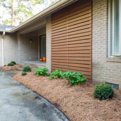 After photo showing stained outdoor modern wood slat accent wall on brick Ranch home.
