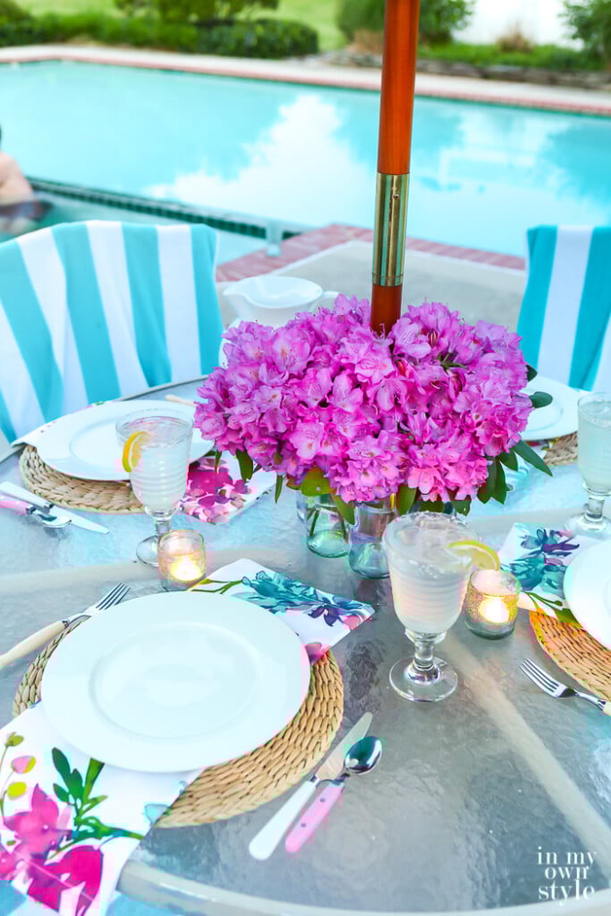 faux flower centerpiece on a round outdoor table with an umbrella pole in the center of the table.
