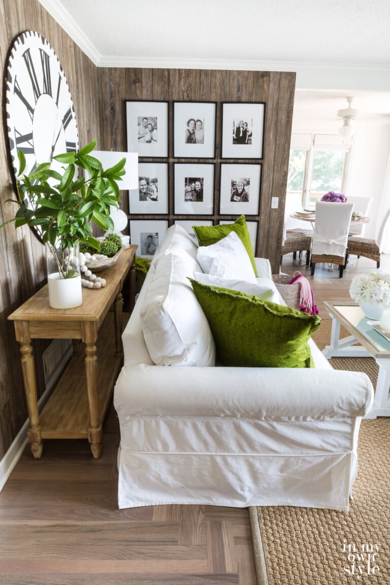 Faux barnwood paneled wall in living room with photo gallery, white sofa with green pillows and seagrass rug.