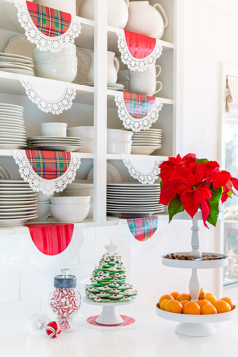 White kitchen with open shelves. Red plaid doilies hanging from the shelves.