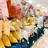 Toss pillows on display in the aisle at Home Goods in the colors yellow, blue and orange.