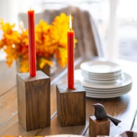 Completed DIY Wooden Candle Holders on a dining table with dark orange taper candles.