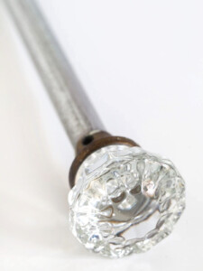 Glass doorknob attached to metal pipe to create DIY curtain rods.