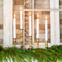 A group of brass candlesticks and white candles on mantel decorated for Christmas