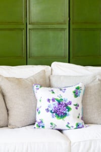 Linen pillow with violets on a sofa with a decorative screen behind it painted green with glaze and dark wax.