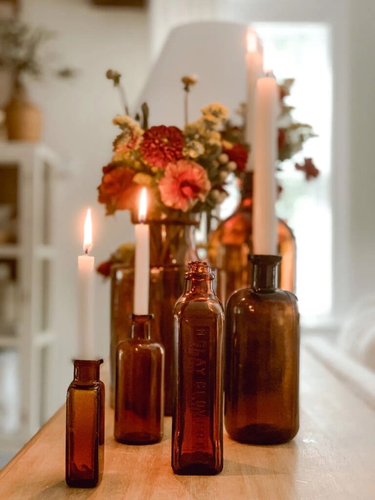 a collection of amber bottles with candles and flowers in them.