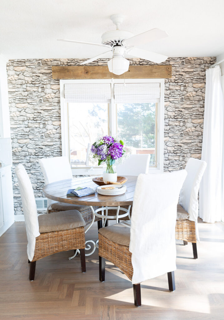 Kitchen table with 5 dining chairs around it each with a white slipcover.