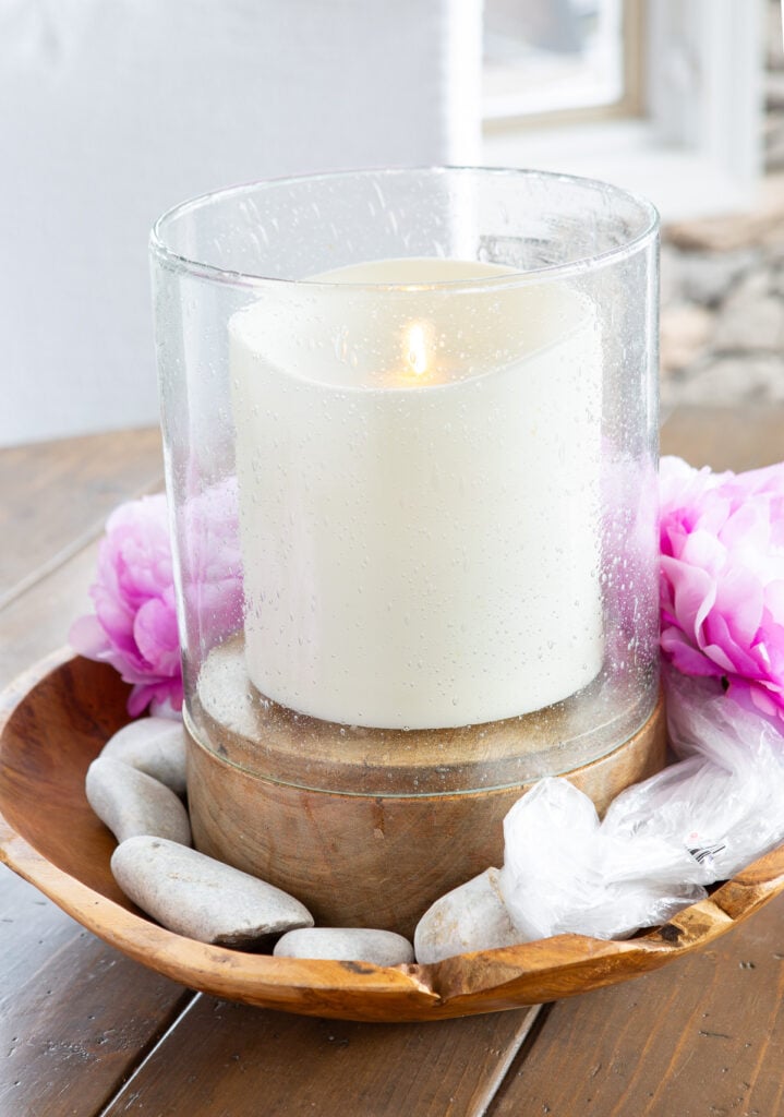 wood bowl filled with a large candle, rocks and flowers to create an Easter table centerpiece.