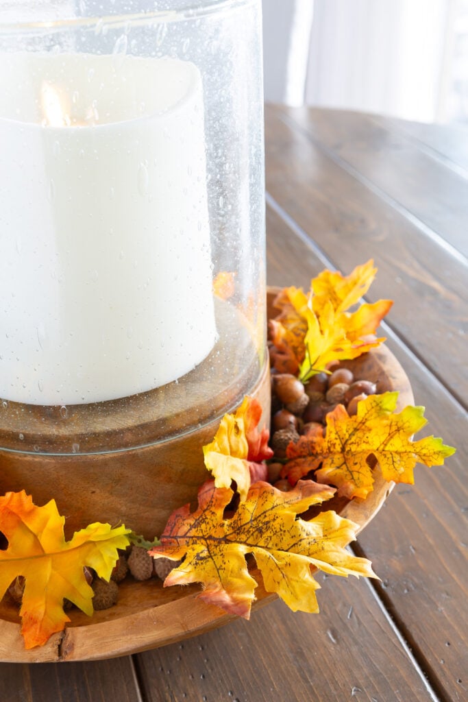 single faux fall leaves around a candle in a wood bowl