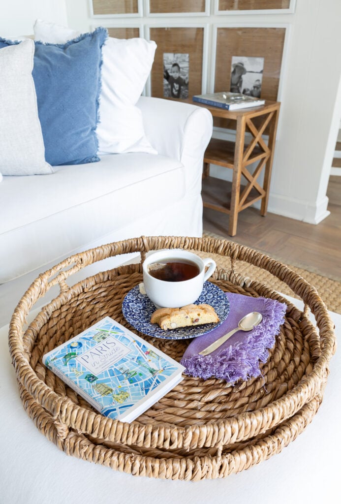 Looking down at a round rattan tray holding a cup of tea, napkin and spoon, a biscotti and a book.