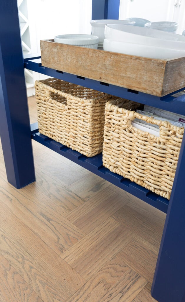 View of bottom shelf on small kitchen work table island with two baskets on it.