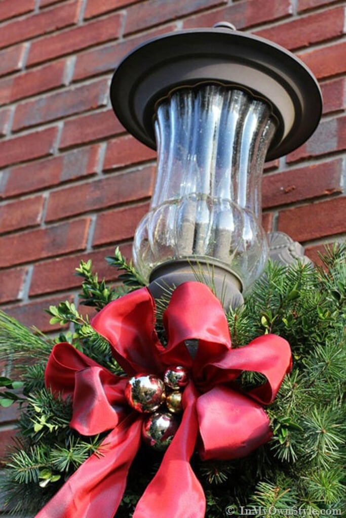 close up of an exterior front porch light decorated for Christmas using real greenery and red ribbon.