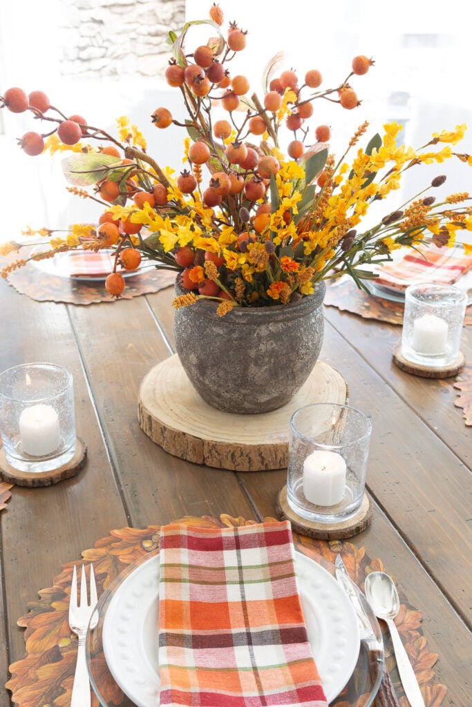 Thanksgiving table centerpiece on the middle of a round wood table set for Thanksgiving dinner.