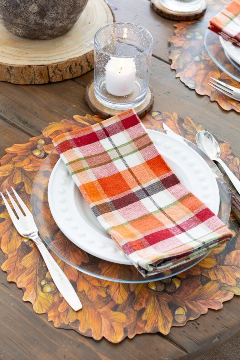 Thanksgiving table setting with a Hester & Cook fall leaves paper placemat and plaid napkin on glass plate.