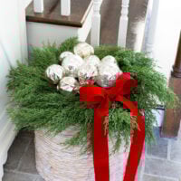 A collection of silver ornaments nestled in a wreath on top of a large woven floor basket.