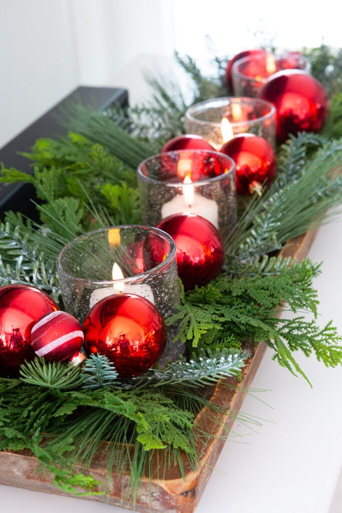 a dough bowl decorated for Christmas with greenery, glass candles votives and red ball ornaments.