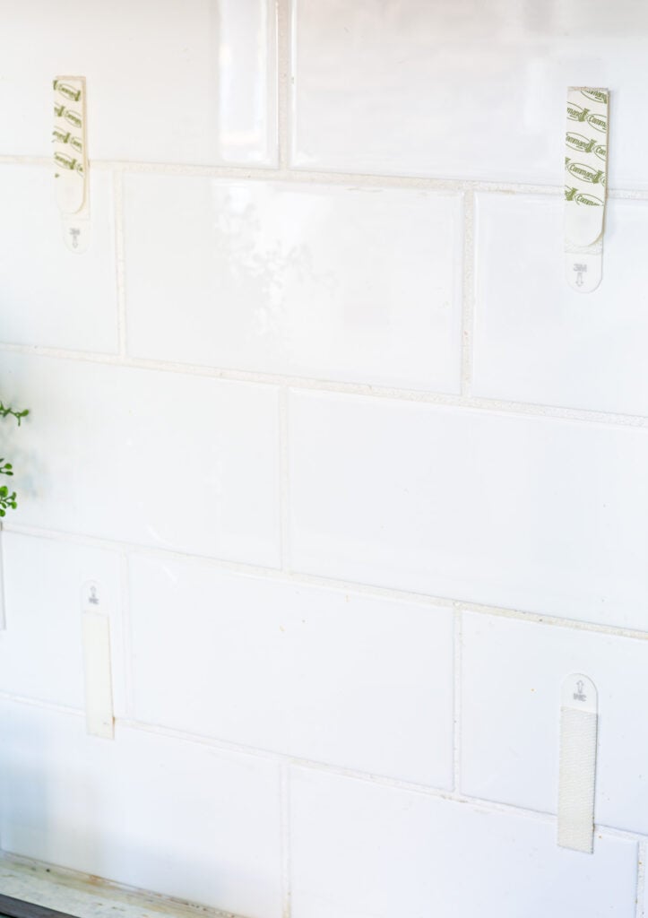 Command Brand picture hanging strips attached to tile backsplash in a kitchen ready to hang framed art.
