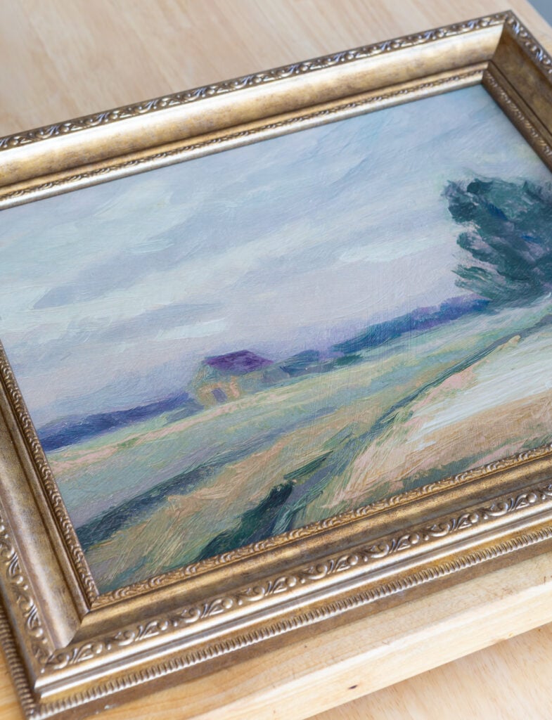 Looking down at framed art with a landscape done in soft greens, blues and purple.