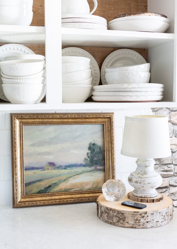 Looking at a kitchen counter where framed art is leaning against a white tile backsplash.