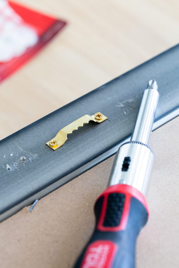 screwdriver removing a picture hanging bracket on the back of a wood frame