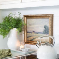 framed artwork hung on white tile backsplash in kitchen. Stove and teapot nearby.