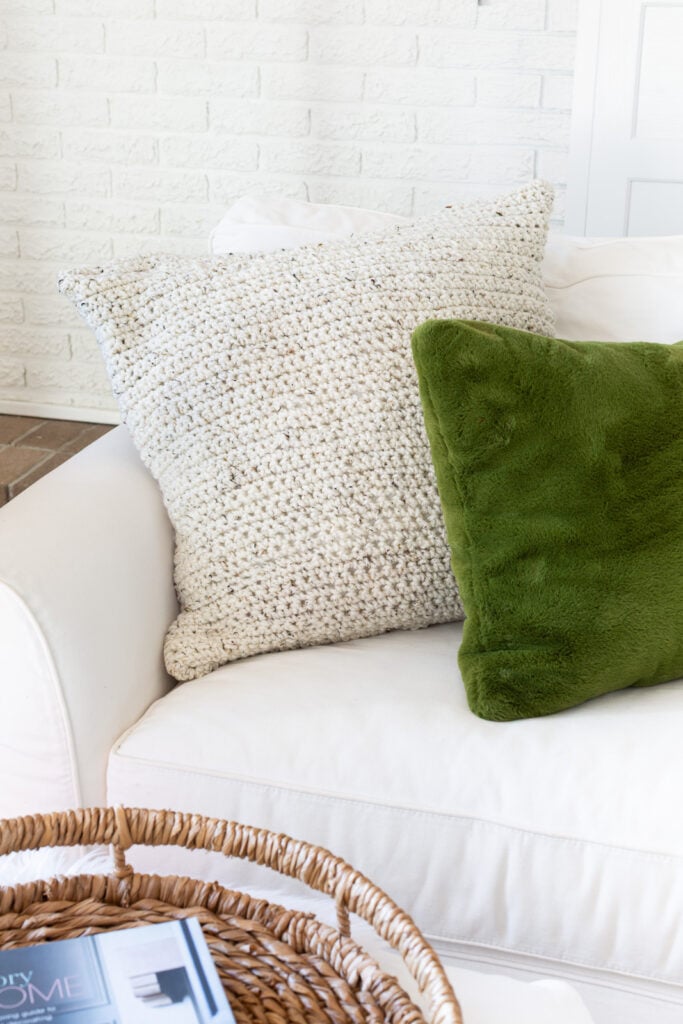 cream colored crocheted pillow on white sofa with a green pillow nearby