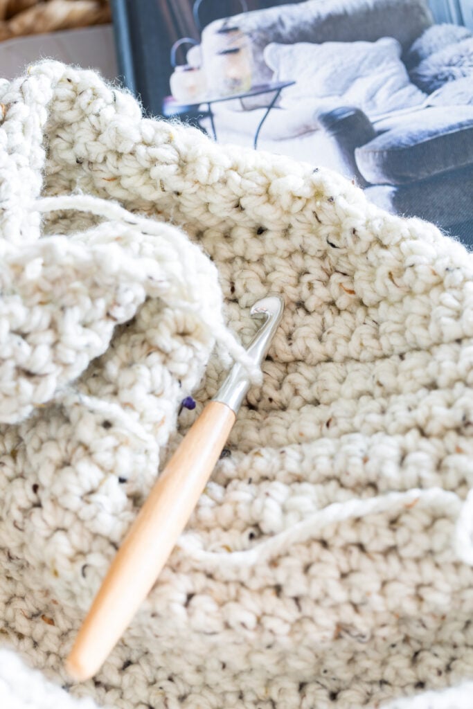close up of a pillow cover showing crochet stitch texture and a crochet hook