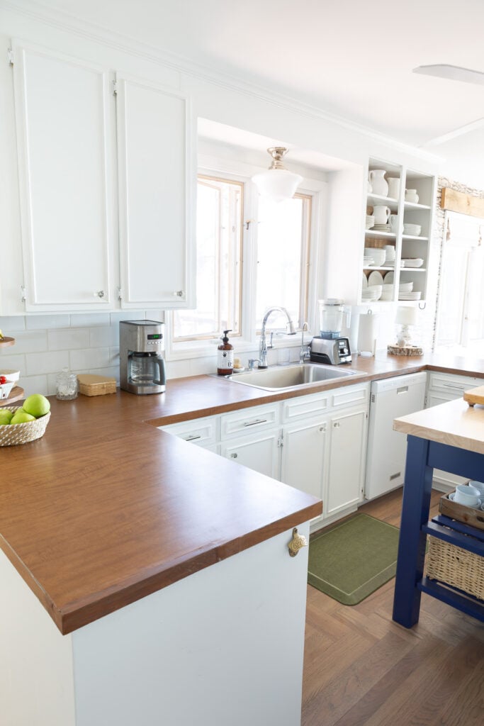 Looking a sink area in kitchen with white cabinets and brown Formica counters