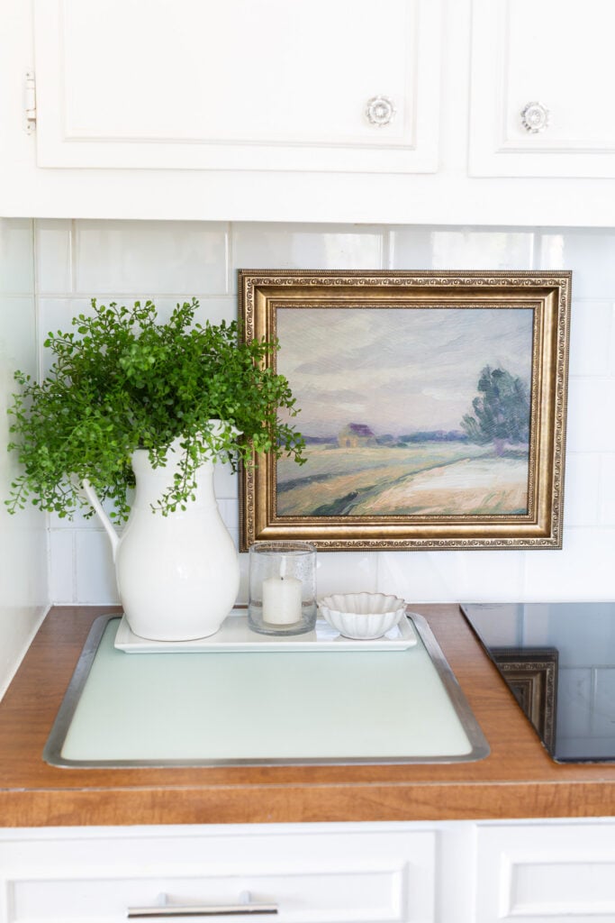 kitchen counter with vintage bulit-in glass cutting board with a landscape painting hanging on the tile backsplash.