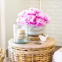 Corner of living room with a rounf wicker basket table with a faux concrete planter filled with faux peonies for early spring decor.