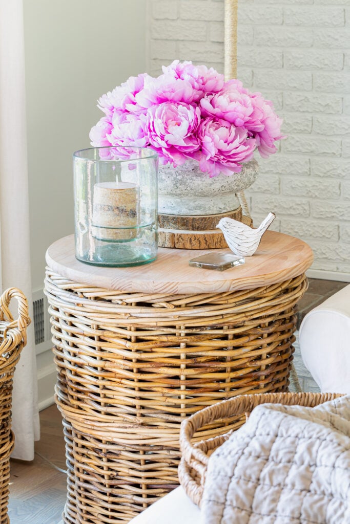 Corner of living room with a rounf wicker basket table with a faux concrete planter filled with faux peonies for early spring decor.