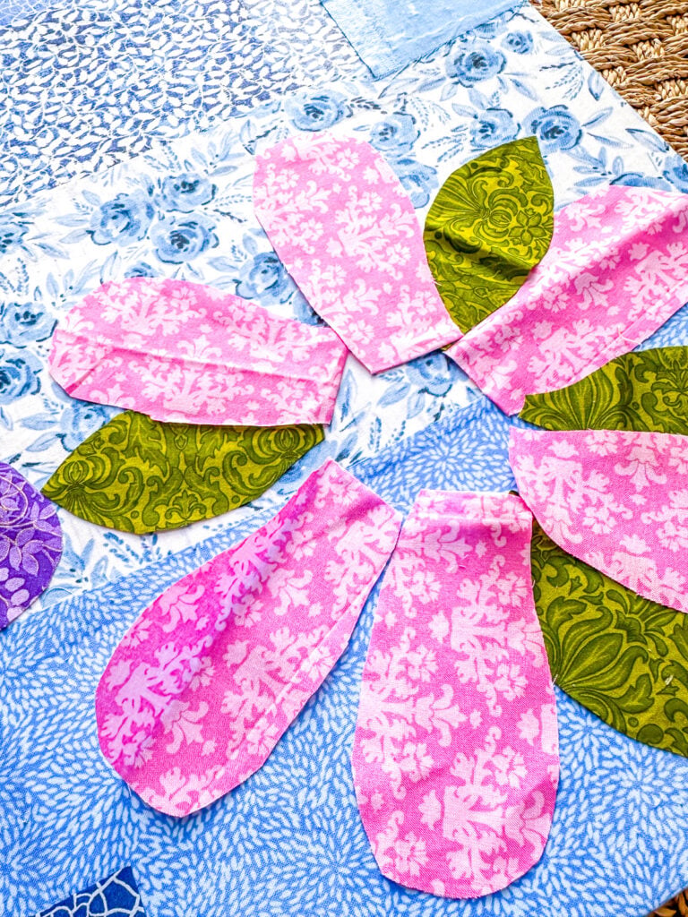 Placing cut out flower petal shapes on fabric strip covered canvas to find appealing layout.