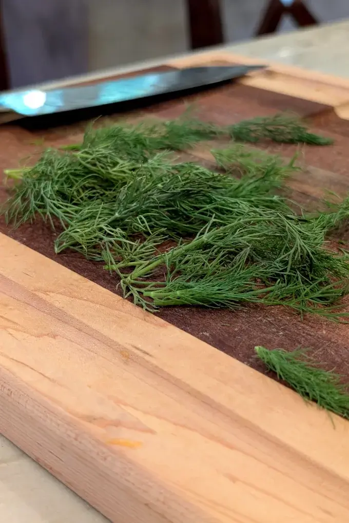 Freshly cut dill on a cutting board with a knife in the background