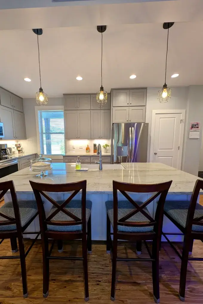 View of kitchen from dining area with chairs under a countertop and cabinets and appliances in the background