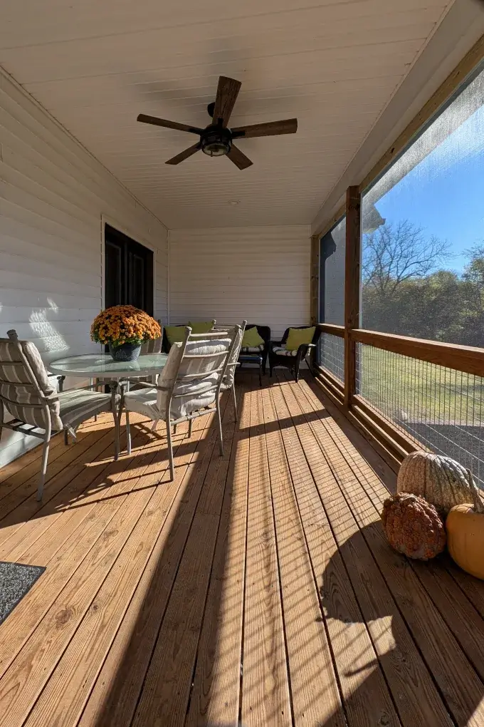 A screened in deck with a table and some fall decorations