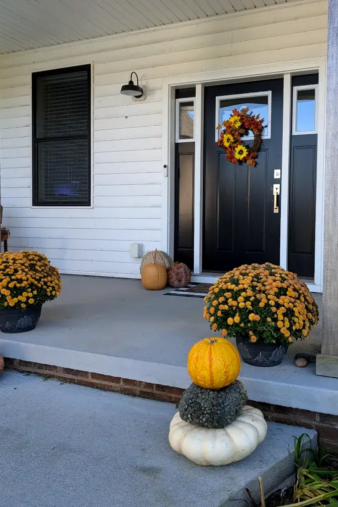 Front porch with pumpkins and mums and a black entrance door